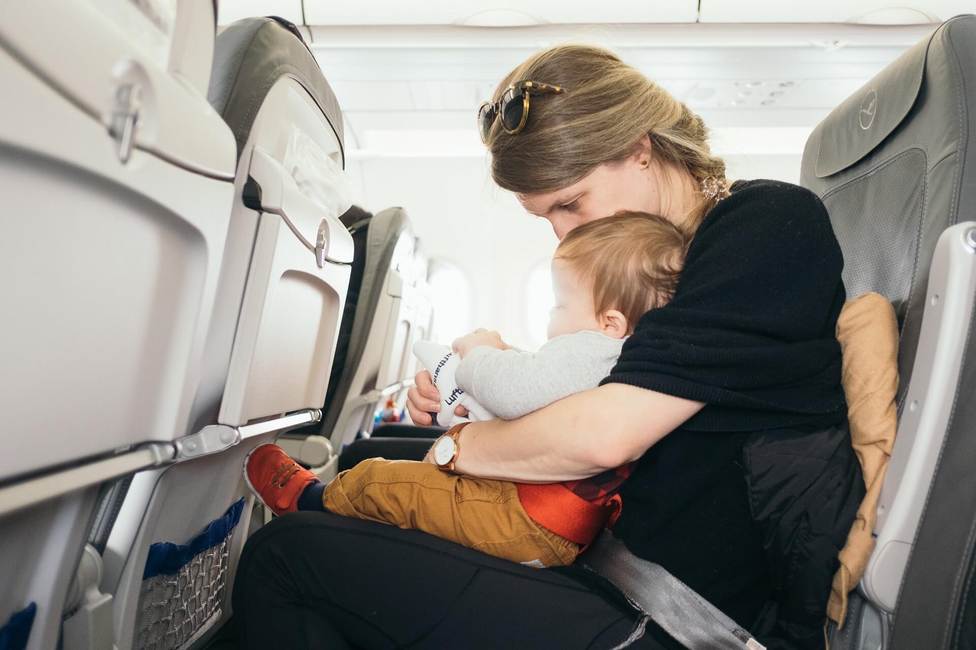 Stressfrei zum Flughafen mit den Kindern? Ganz easy mit McParking am Flughafen BER Mutter im Flugzeug mit Baby auf dem Schoß