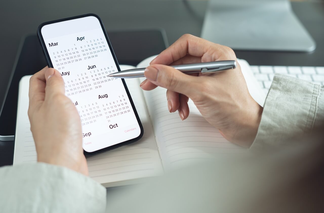 Žena drží v ruce mobilní telefon a v telefonu je otevřený kalendář.