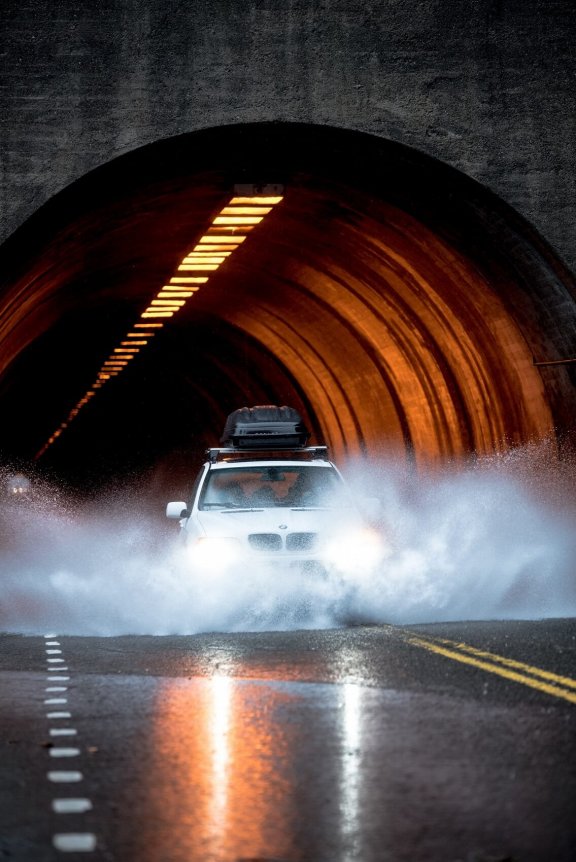 Car with roof luggage drives through large puddle