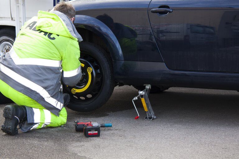 Mann wechselt Reifen am Auto