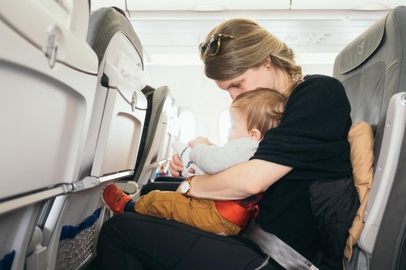 A woman sits on a plane with a baby on her lap