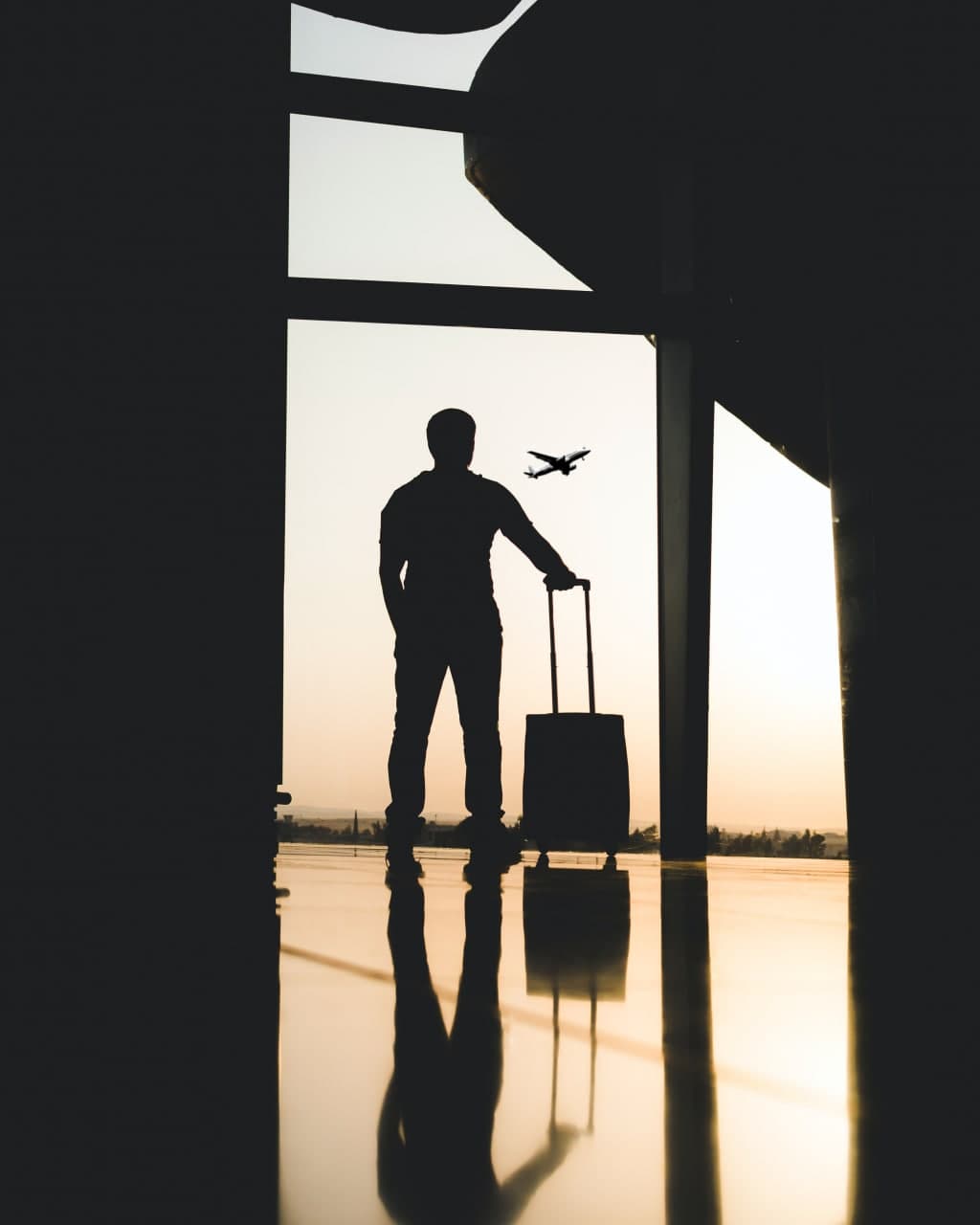 Man with suitcase looks out of the window at the airport towards the plane.