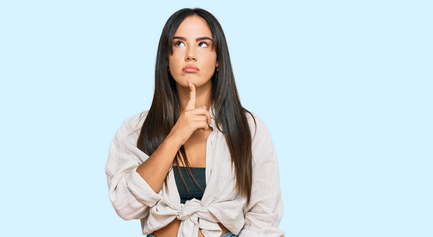 A young, pretty woman with long brown hair looks thoughtfully upward.