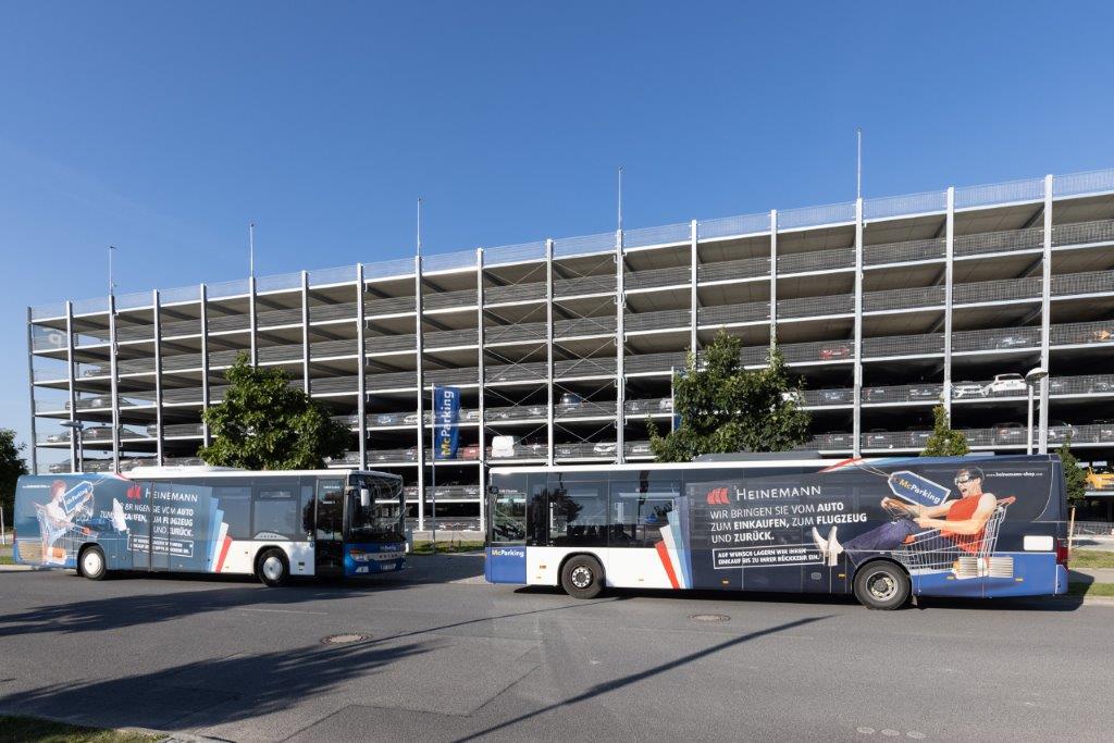 2 large McParking shuttle buses are parked opposite each other in front of the car park.