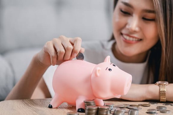 A young woman puts money in a piggy bank