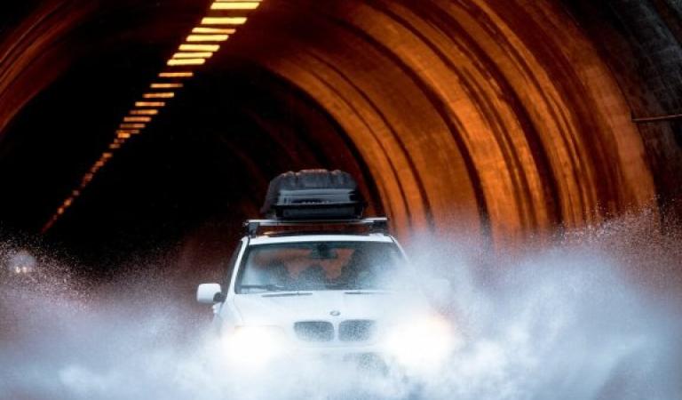 Car with roof luggage drives through large puddle