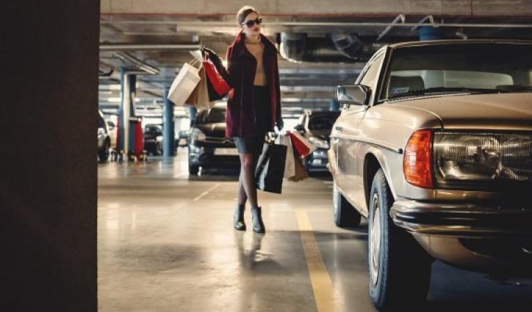 Žena jde s nákupními taškami k autu