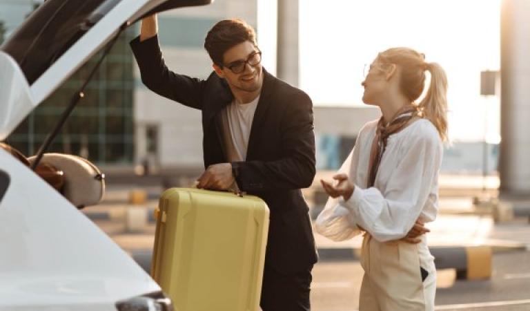 Muž vyndá z auta kufr a mluví se ženou