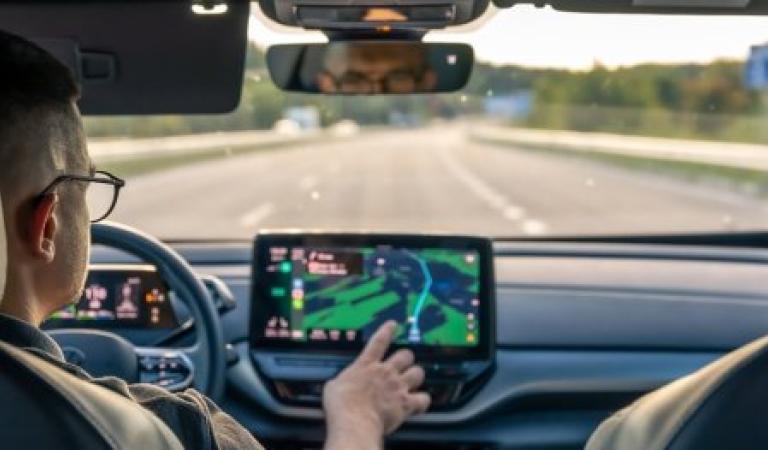 Muž řídí auto na prázdné dálnici a používá navigační systém s dotykovou obrazovkou.